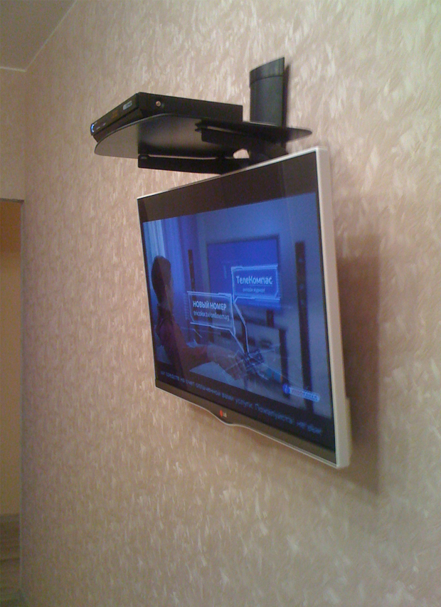 Телевизор на стене с полкой сверху.